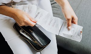 Foto på person med en plånbok i knäet och ett långt kvitto i händerna. 