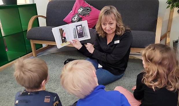 Foto på en kvinnlig pedagog som läser bok för förskolebarn.